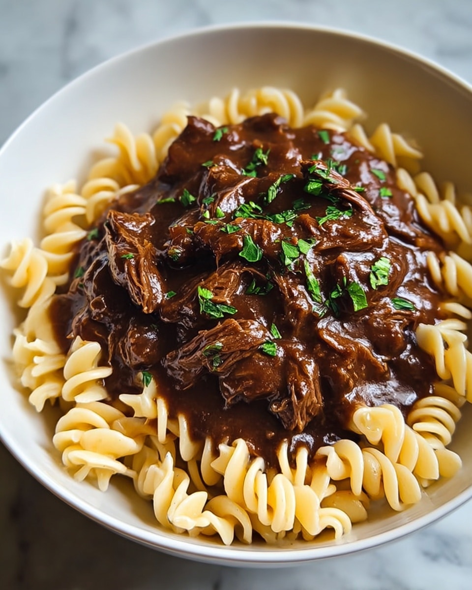 A white bowl sits on a white marbled surface, filled with two visible layers: the bottom layer consists of light yellow spiral pasta with a smooth texture, tightly packed and arranged evenly to fill the bowl; the top layer is a rich, dark brown shredded beef stew with a thick, glossy gravy covering the meat pieces, garnished with small bright green chopped herbs scattered on top, adding a pop of color. The overall look is hearty and rich, with contrasting textures between the soft pasta and tender shredded meat. photo taken with an iphone --ar 4:5 --v 7