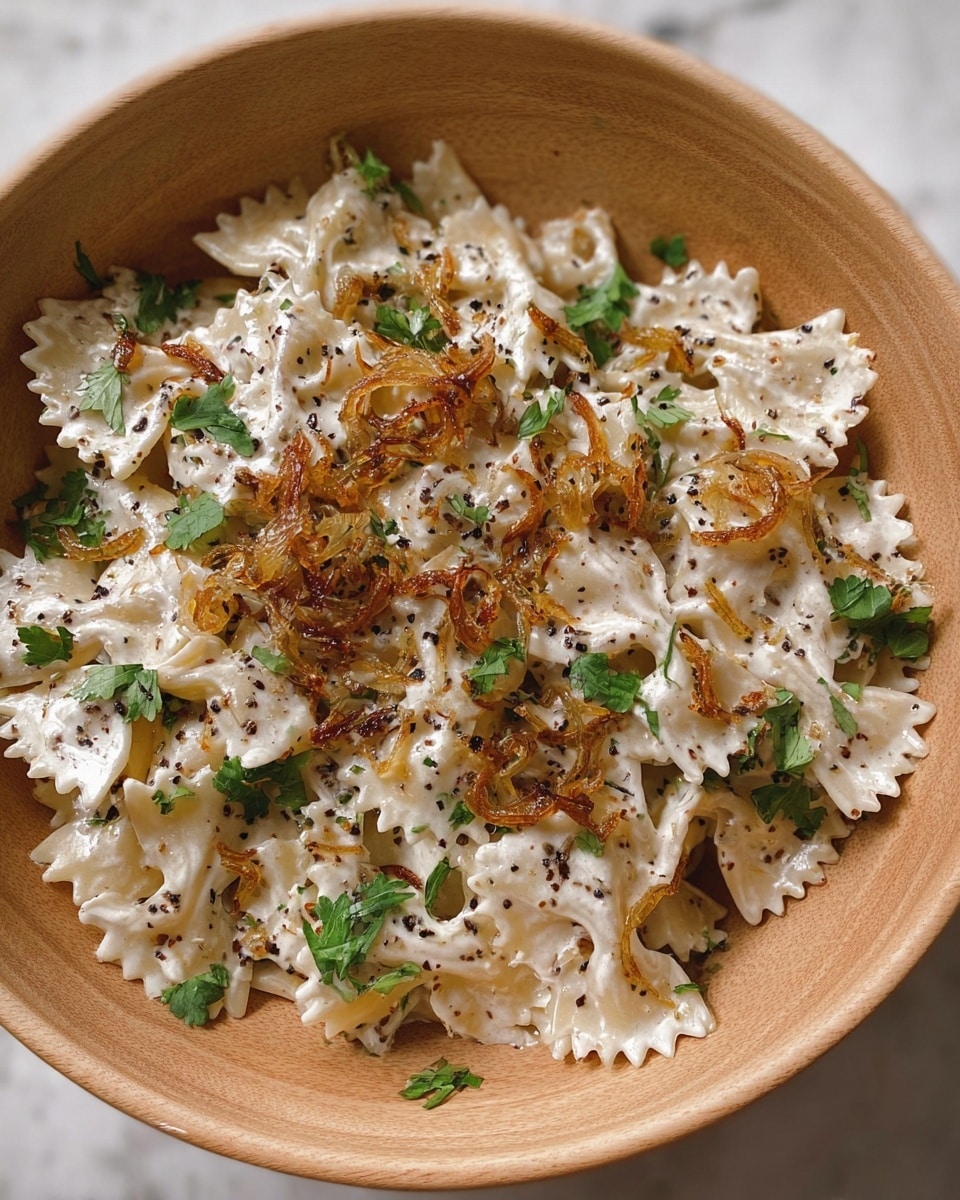 The dish shows a bowl of white farfalle pasta mixed well with creamy white sauce and garnished with dark green cilantro leaves scattered evenly around. On top, there are small piles of golden-brown caramelized onions adding texture and color contrast. The sauce has tiny black pepper specks spread throughout. The pasta is placed in a light wood-textured bowl, and the photo is shot from above on a white marbled surface. photo taken with an iphone --ar 4:5 --v 7