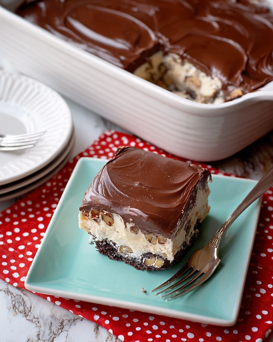 The image shows a square piece of layered dessert on a white square plate with a shiny mint green plate below it, placed on a red cloth with white dots over a white marbled texture. The dessert has three main layers: a bottom layer of dark chocolate with visible nuts, a middle creamy beige layer with small dark bits, and a top smooth and glossy chocolate frosting layer. The dessert is thick and the frosting is evenly spread with soft swirled patterns. Next to the plated piece is a white baking dish with the rest of the dessert, showing the inside layers with some missing where the piece was cut. A fork rests near the plate. Photo taken with an iphone --ar 4:5 --v 7