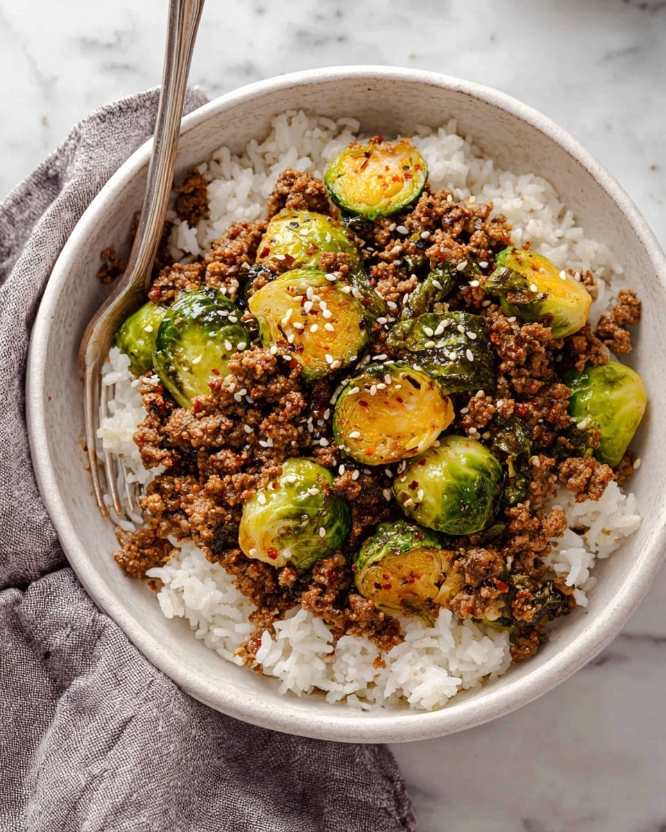 A white bowl holds two layers: the bottom layer is fluffy white rice with grainy texture, evenly spread; the top layer is a mix of browned ground meat and bright green Brussels sprouts, some halved and showing a slightly charred yellow inside, scattered over the rice. Small white sesame seeds sprinkled on top add texture, and a silver fork rests on the left edge of the bowl, partially touching the food. The bowl sits on a white marbled surface with a soft gray cloth nearby. Photo taken with an iphone --ar 4:5 --v 7