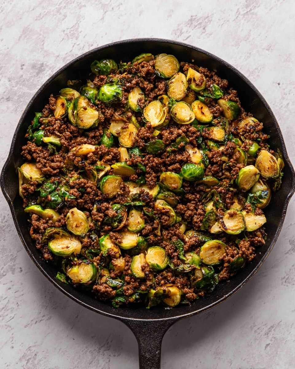A black cast iron skillet filled with a cooked mix of browned ground meat and halved, sautéed Brussels sprouts scattered evenly throughout. The Brussels sprouts have a bright green color with some parts caramelized to a golden-brown, and the meat is dark brown with a crumbly texture. The skillet sits on a white marbled surface that is clean and smooth, emphasizing the rich colors of the cooked ingredients inside the pan. photo taken with an iphone --ar 4:5 --v 7