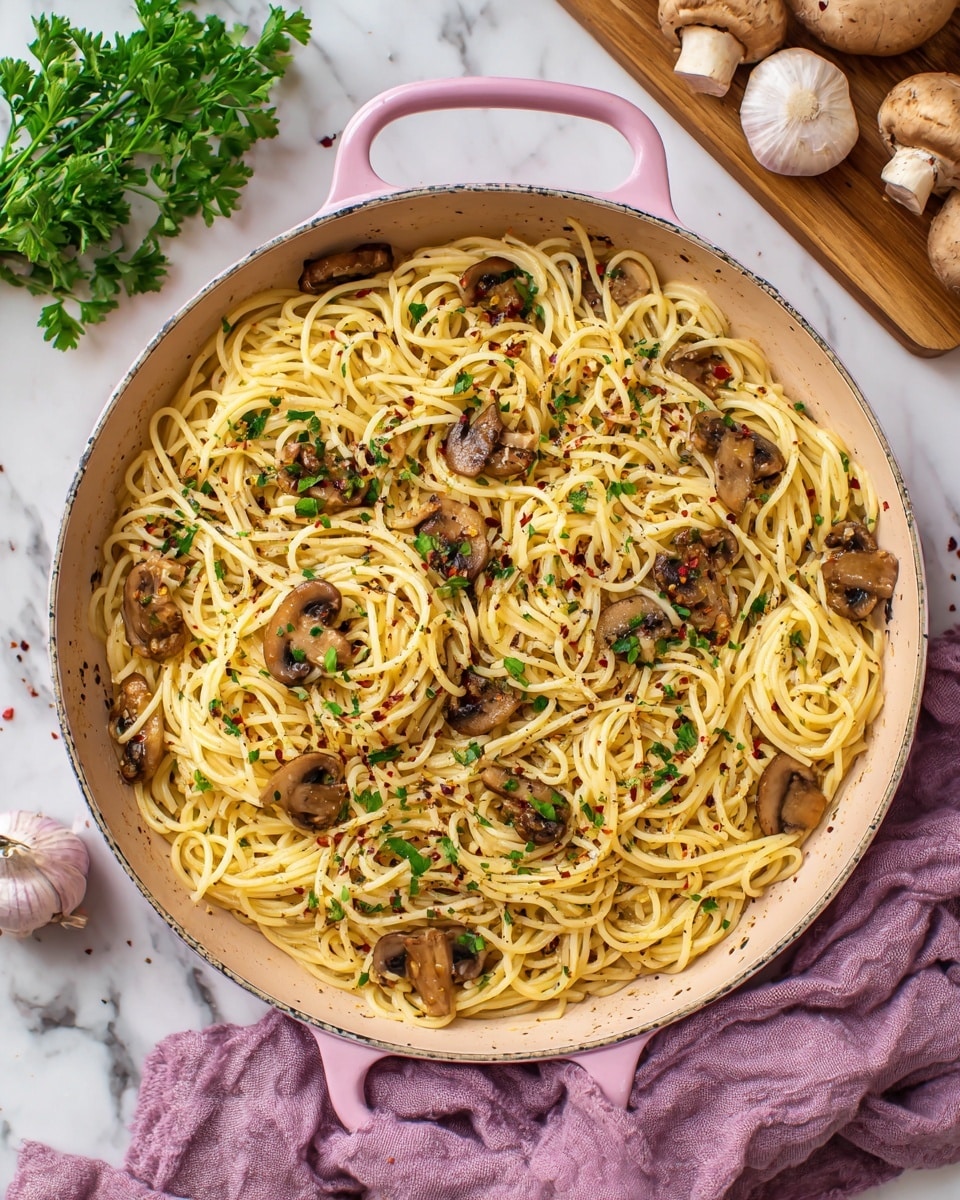 A pink skillet filled with a dish of spaghetti noodles mixed with sautéed brown mushroom slices and small green parsley leaves. The spaghetti is pale yellow with a smooth texture, while the mushrooms add a slightly glossy and dark brown contrast scattered evenly throughout. Some crushed red pepper flakes and small bits of black pepper are sprinkled on top. The skillet sits on a white wooden surface next to a light purple cloth napkin, with a cutting board holding whole mushrooms, garlic, and parsley blurred in the background, all on a white marbled texture. Photo taken with an iphone --ar 4:5 --v 7