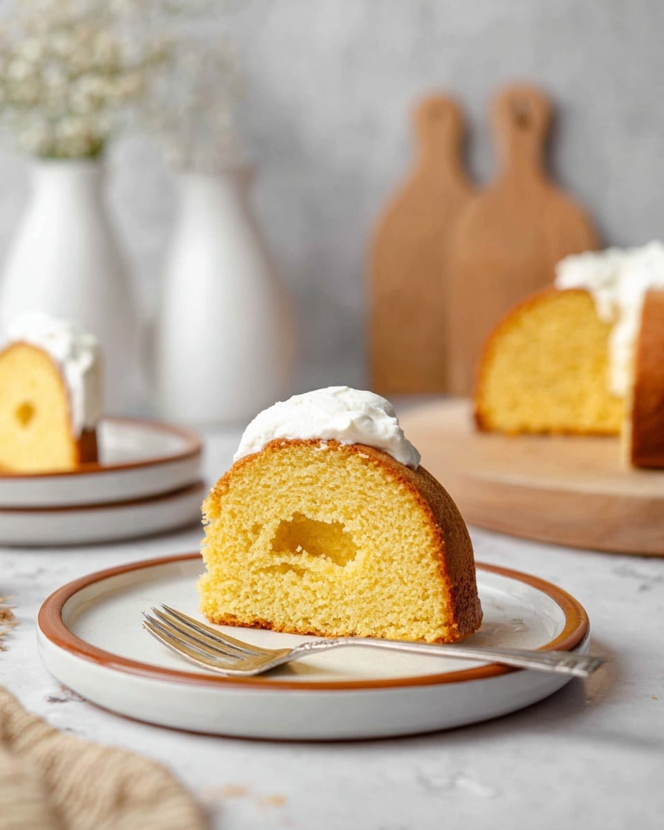 A slice of golden yellow cake with a soft and moist texture sits on a white plate with a brown rim. The cake is a single layer with a hollow center filled with smooth white cream. A silver fork lies beside the cake on the plate. In the background, there are more slices of the same cake on white plates with brown rims, wooden cutting boards, and white vases on a white marbled surface, creating a clean and simple setting. photo taken with an iphone --ar 4:5 --v 7