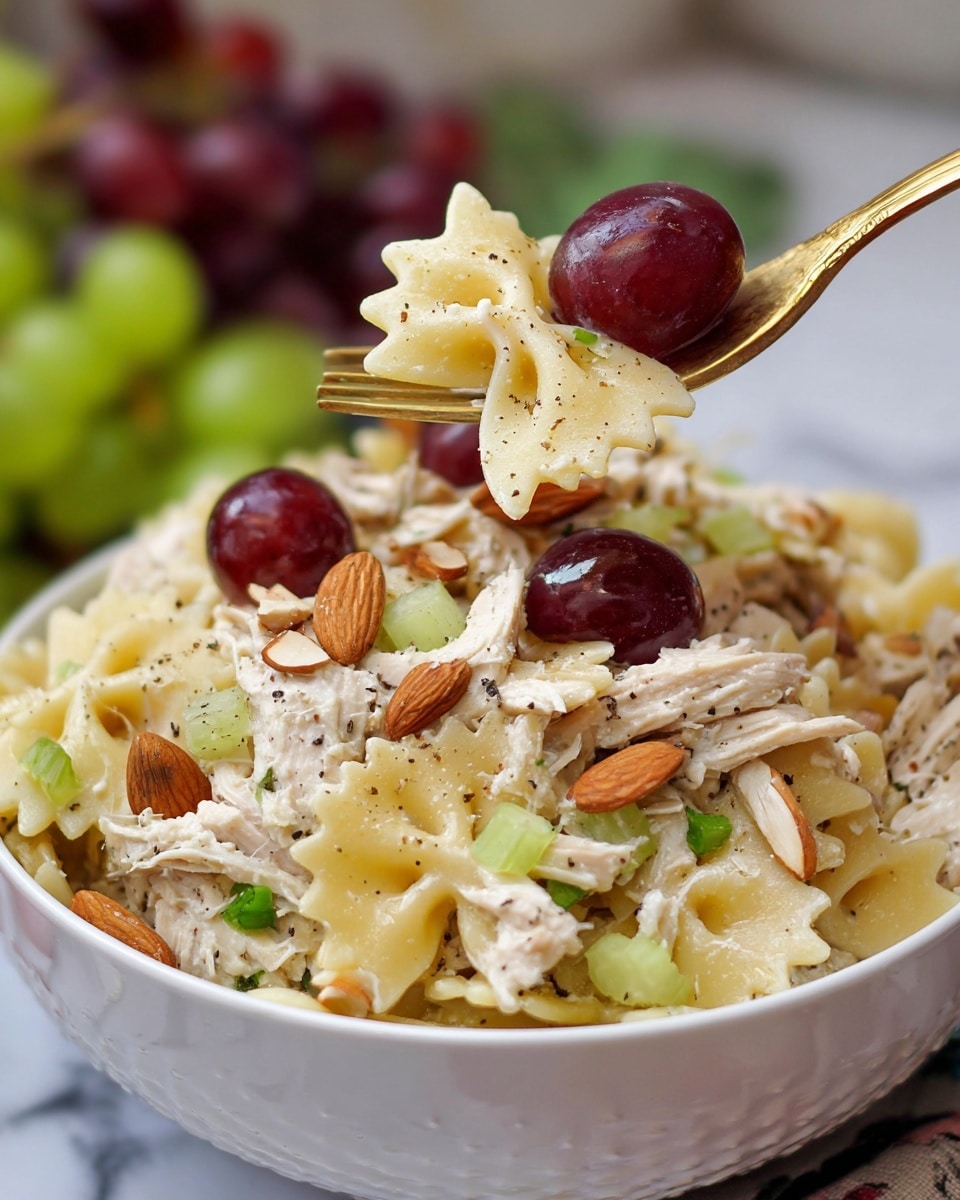 A white bowl filled with a colorful pasta salad is shown close up on a white marbled surface. The salad has three main layers: the base layer is light yellow bowtie pasta with a smooth texture, mixed with diced pale green celery pieces. On top of the pasta, there is shredded white chicken seasoned with small black pepper specks, giving it a slightly speckled look. Scattered throughout the salad are whole dark red grapes providing a smooth and glossy contrast. Thinly sliced, light brown toasted almonds add a crunchy texture on top. A woman's hand is holding a fork that is lifting some pasta, chicken, a grape, and celery pieces from the bowl. In the blurry background, some greenery and additional grapes are visible. photo taken with an iphone --ar 4:5 --v 7