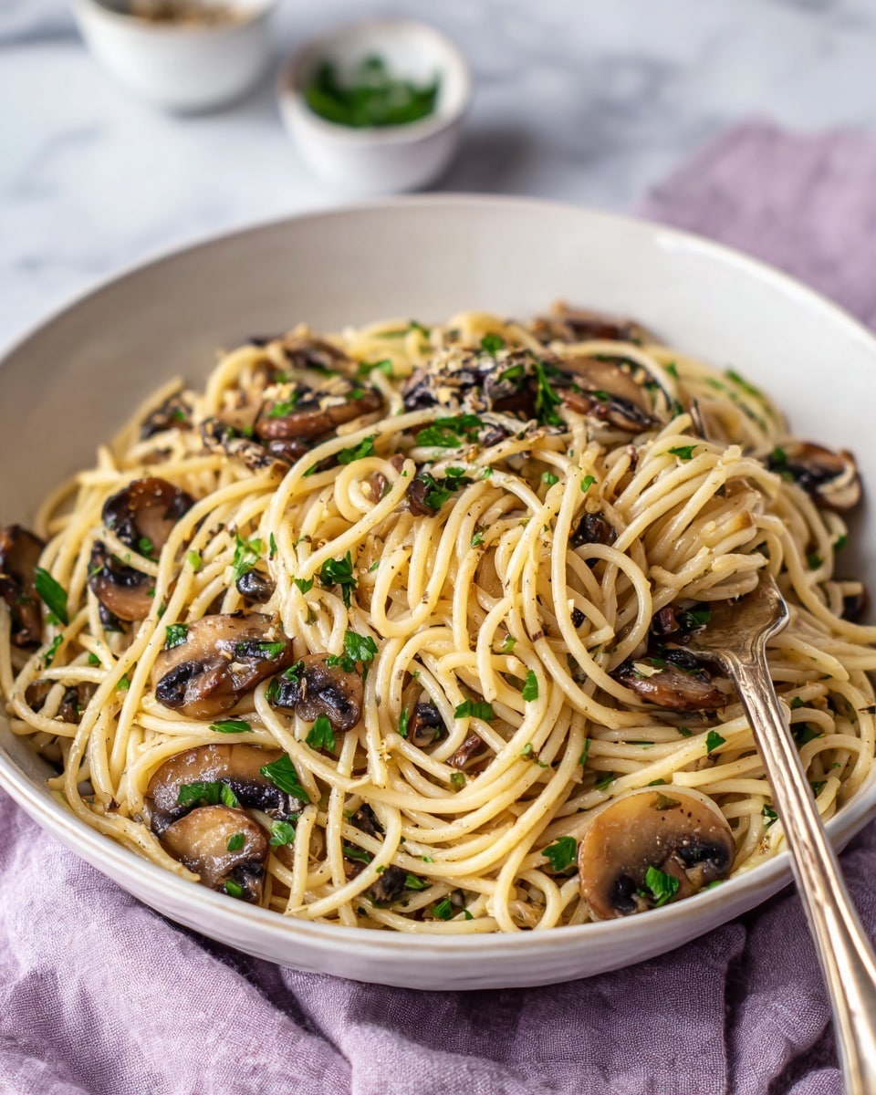 A white bowl filled with light beige cooked spaghetti noodles twisted and piled high, mixed with dark brown sautéed mushroom slices and small bright green parsley leaves scattered throughout. A silver fork rests inside the bowl, twirling some spaghetti around its tines on the right side. The bowl sits on a soft light purple cloth, all placed on a white marbled texture surface. Blurred small white bowls sit in the background adding depth. Photo taken with an iphone --ar 4:5 --v 7