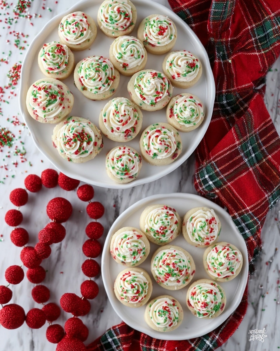 The image shows two white plates filled with small round cookies decorated for the holidays. Each cookie has a base layer of soft-colored dough with red and green specks inside. On top of each cookie, there is a swirl of white creamy frosting in the center, decorated with red and green sprinkles scattered over the frosting. The larger plate holds about 20 cookies arranged close together, and the smaller plate holds 8 cookies placed in a circle. The plates rest on a white marbled surface with a red and green plaid cloth partially under the smaller plate, and a red felt ball garland is loosely arranged around the plates. Photo taken with an iphone --ar 4:5 --v 7