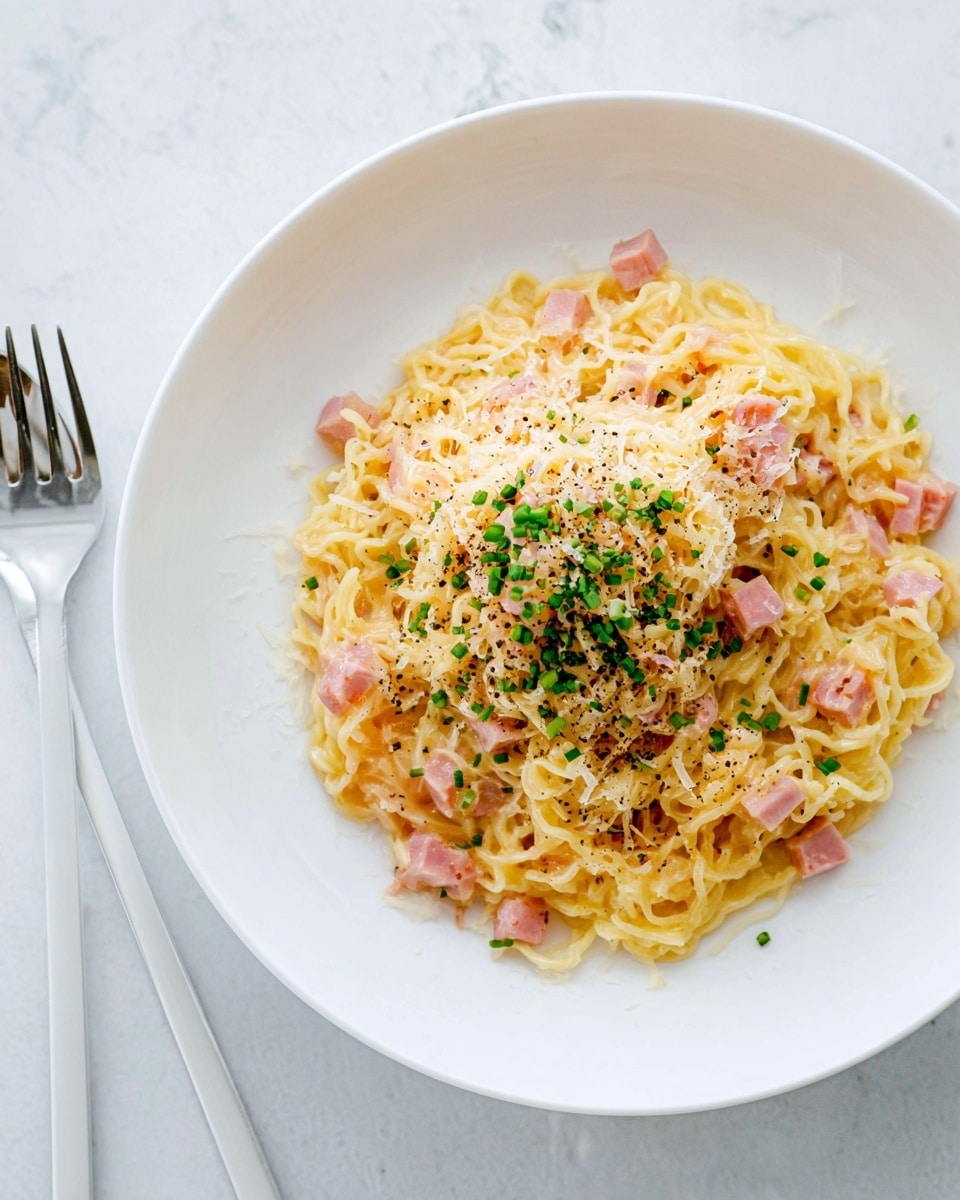 A white plate holds a single layer of cooked yellow noodles, soft and tangled, covering the center. Mixed in are small pink ham pieces spread evenly throughout the noodles. On top, a layer of grated pale yellow cheese lightly dusts the noodles, sprinkled with black pepper flakes. Green chopped chives are scattered in the middle, adding a fresh color contrast. The plate sits on a white marbled surface, and a white fork lies beside it. photo taken with an iphone --ar 4:5 --v 7