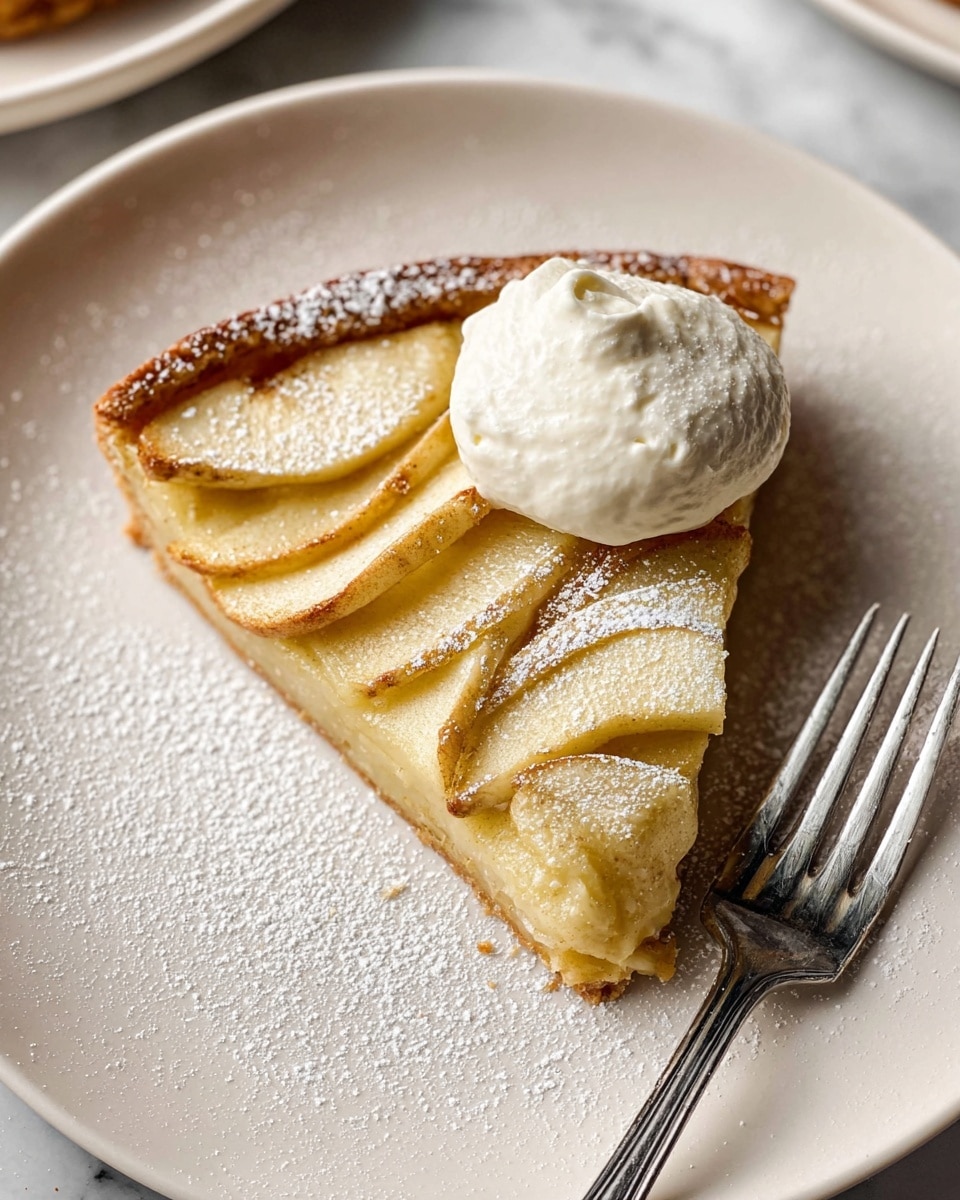 A slice of light golden brown tart with thin, evenly layered slices of pale yellow apple arranged on top, dusted lightly with powdered sugar, sits on a white plate. The tart has a slightly crisp crust around the edge. On top of the apple layer is a dollop of smooth, white whipped cream. To the right of the tart slice, there is a silver fork resting on the plate. The plate is placed on a white marbled surface. Photo taken with an iphone --ar 4:5 --v 7