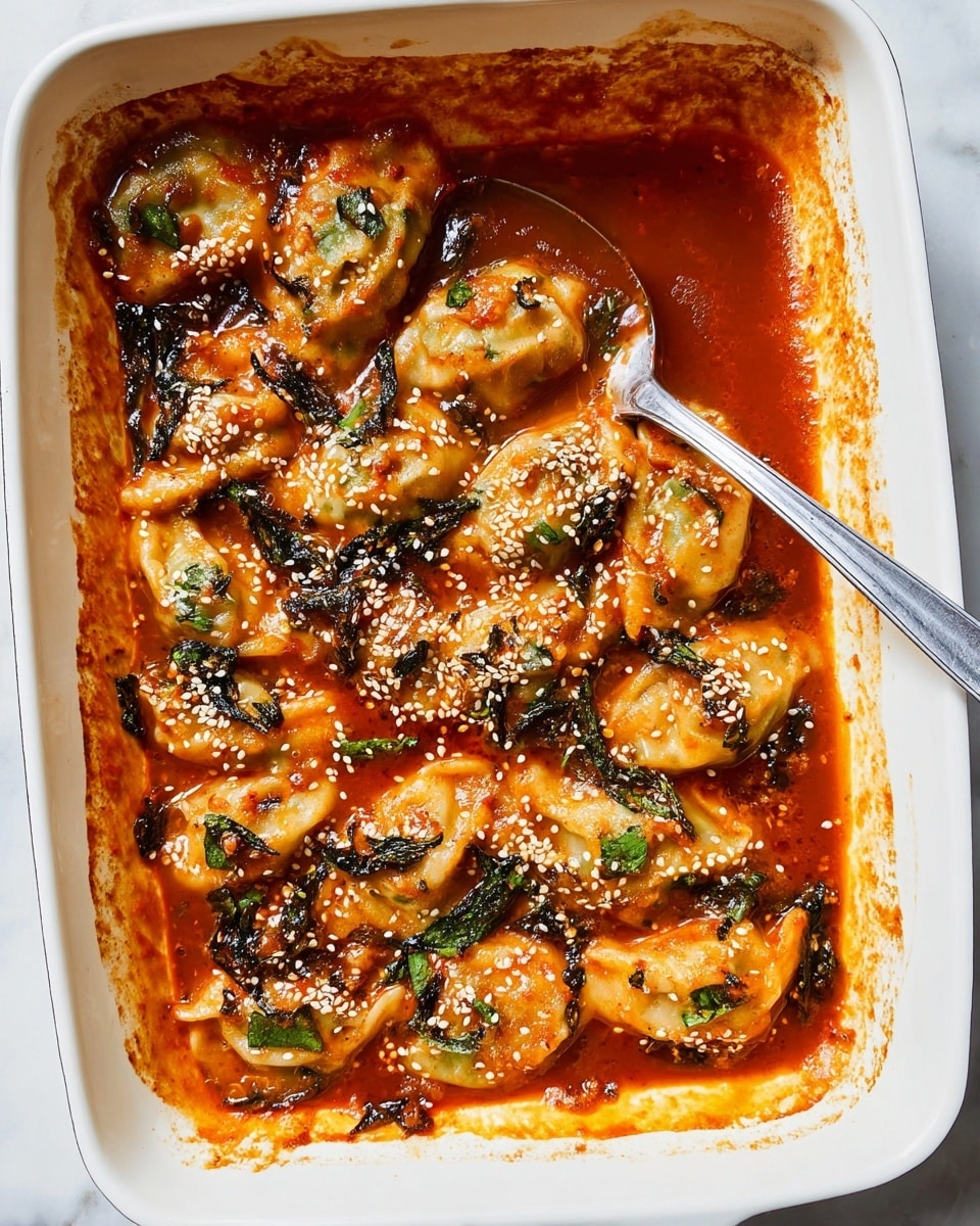 A white rectangular baking dish holds a layer of plump dumplings covered in a rich reddish-orange sauce. The dumplings are arranged in overlapping rows, their soft, slightly wrinkled skins visible under the sauce. Dark green leafy herbs are scattered throughout, adding texture and color contrast. White sesame seeds and small green herb bits are sprinkled evenly over the top. A silver spoon rests inside the dish, coated with the thick sauce. The edges of the dish show slight browning from baking. The dish sits on a white marbled surface. Photo taken with an iphone --ar 4:5 --v 7