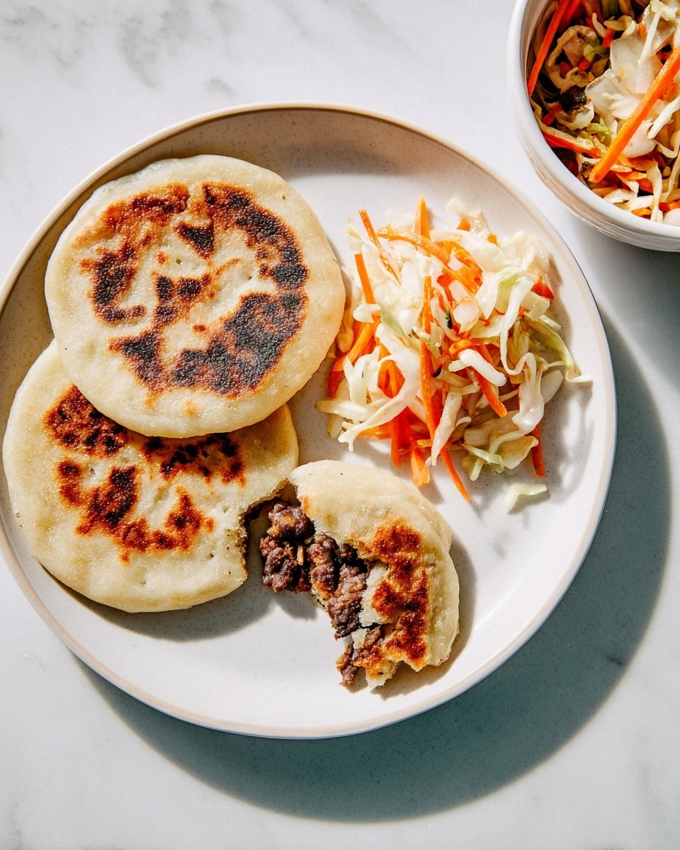 The image shows a white plate with two round flatbreads, one whole and the other with a bite taken, revealing a dark, chunky filling inside made of black beans and other ingredients. Next to the flatbreads is a side of mixed pickled vegetables, including shredded white onions, carrots, and cabbage in light orange, white, and pale green colors with a slightly wet texture. In the top right corner, there is a white bowl filled with the same mixed pickled vegetables. The entire setup is on a white marbled surface. photo taken with an iphone --ar 4:5 --v 7