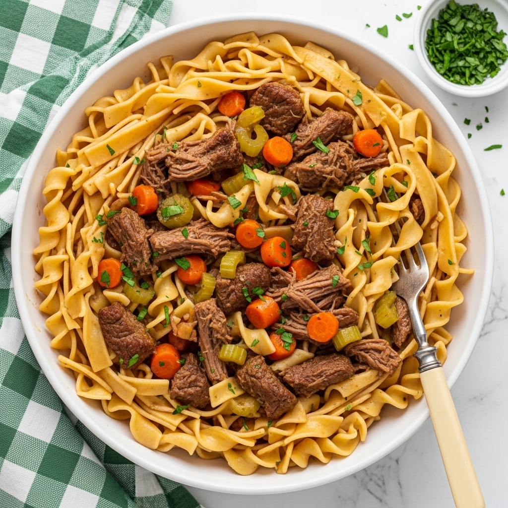 A large white bowl filled with wide, curled egg noodles layered evenly throughout the dish, mixed with chunks of tender brown shredded beef and small cubes of orange carrots and light green celery. The dish is coated in a glossy, rich brown sauce combining all ingredients, with fresh green parsley sprinkled on top. A vintage silver fork with a cream-colored handle rests inside the bowl, partially buried in the noodles and beef. The bowl sits on a white marbled surface next to a green and white checkered cloth and a small bowl of chopped herbs nearby. Photo taken with an iphone --ar 4:5 --v 7